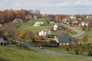 A scenic view of a suburban neighborhood in Southwest Ohio, featuring large homes on rolling hills surrounded by autumn-colored trees and spacious lawns.