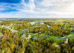 Aerial view of a rural community in Northeast Ohio, showing a landscape of green fields, winding roads, and houses surrounded by trees under a blue sky with clouds.